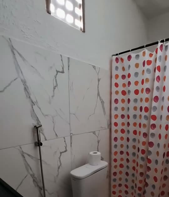 Banheiro da Kitnete Família, com revestimento claro, ducha e cortina de bolinhas vermelhas.