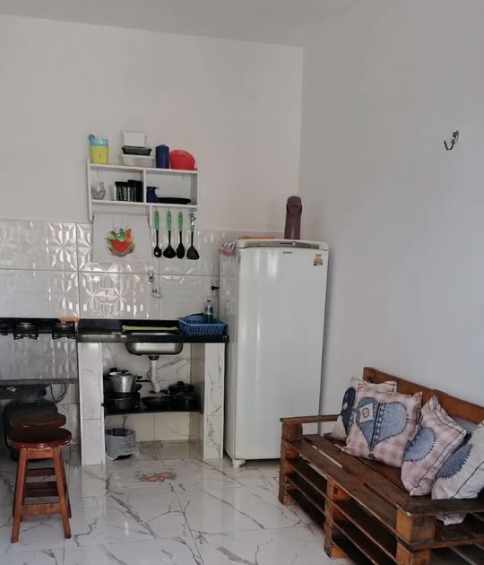 Cozinha da Kitnete Família, com geladeira, cooktop, prateleira de temperos, sofá de pallet e banqueta de madeira.