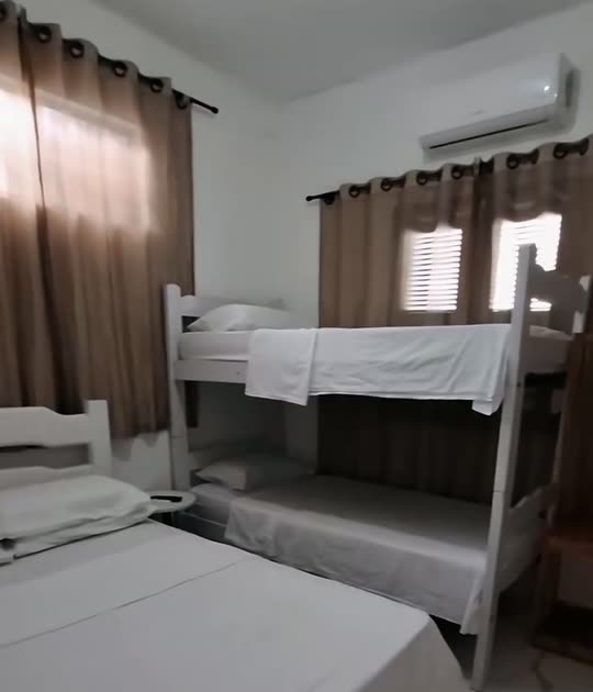 Quarto da Kitnete Família, com beliche e cama de solteiro, ar-condicionado de parede e cortinas bege.