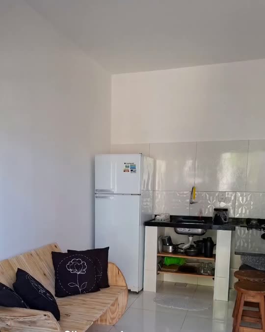 Cozinha da Kitnete Top, com geladeira, cooktop sobre bancada preta, sofá de pallet e piso claro.