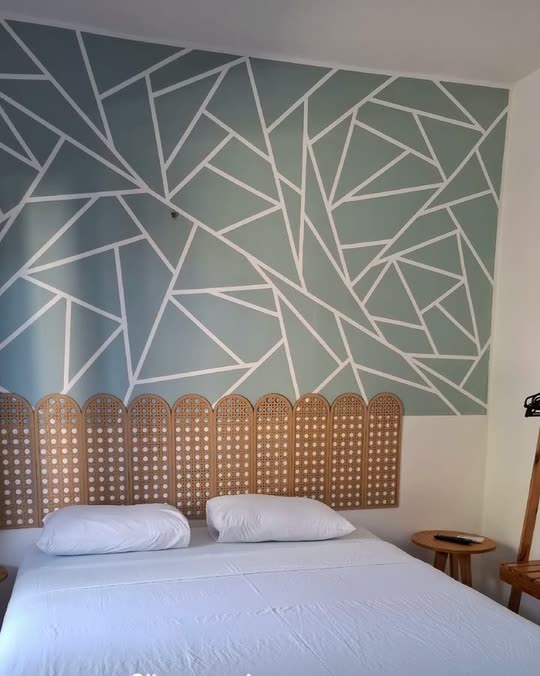 Quarto da Kitnete Top, com cama de casal, cabeceira de palhinha e parede pintada com um padrão geométrico verde-claro.