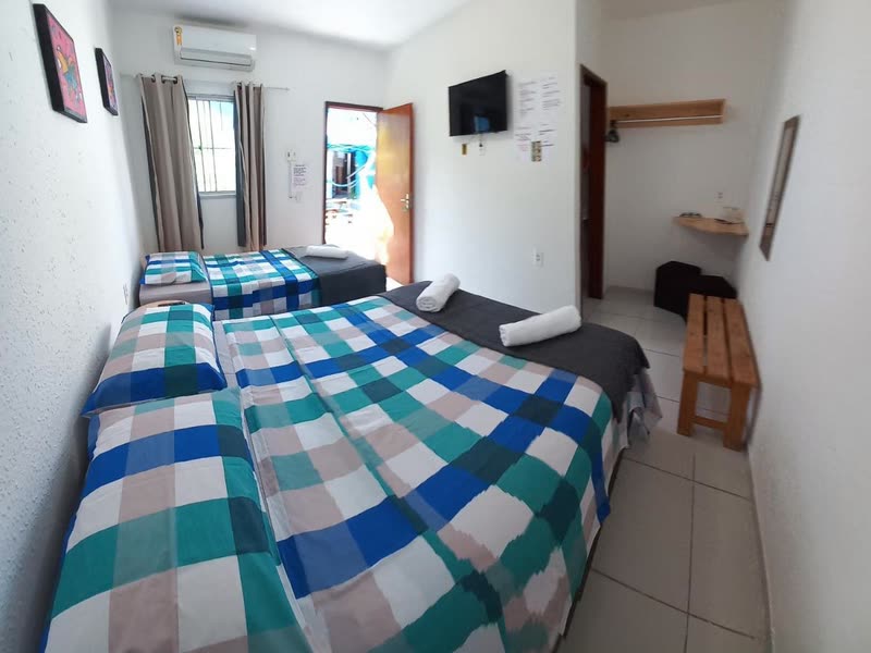 Quarto com duas camas de solteiro lado a lado, colchas xadrez em tons de azul e verde, televisão de tela plana na parede.