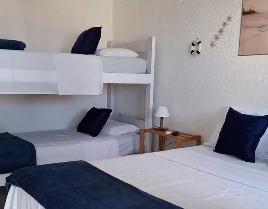 Quarto da Suíte Família, com beliche branco ao lado de uma cama de casal, roupa de cama branca e almofadas azul-marinho.